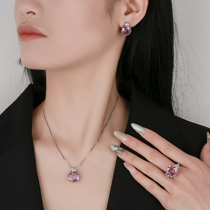Woman wearing pink gemstone jewelry including earrings, necklace, and ring on a neutral background